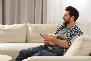Obraz premium Happy man watching TV with popcorn on sofa indoors