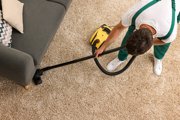 Dry cleaner's employee hoovering carpet with vacuum cleaner indoors, above view