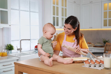 Happy young woman and her cute little baby cooking together in kitchen