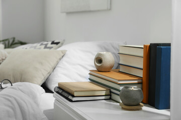 Hardcover books and scented candles on white bedside table in bedroom