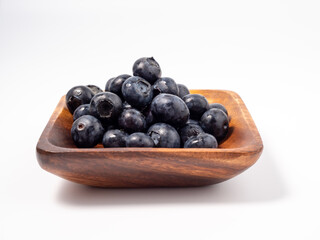 Ripe blueberries in a wooden bowl on a light background. blueberries close up