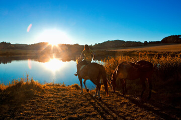 Woman with Two Horses by a Lake at Sunset