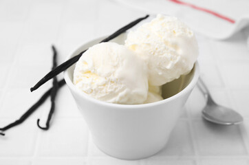 Delicious ice cream and vanilla pods on white tiled table, closeup