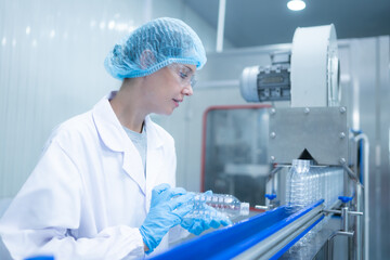 Female quality control worker inspecting water bottle on production line in drinking water factory