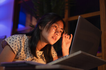 Young Asian female freelancer or student is working late at night. Concept of overload, overworked and burn out of work. Tired, exhausted, fatigue and sleepy from working in front of laptop. Deadline.