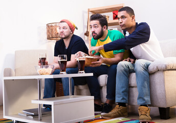 Low view of happy friends watching football game on TV, commenting all moments emotionally and drinking beer with pop corn. © Designpics