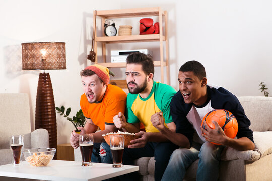 Picture of friends watching football game on TV while spending their weekends at home with alcohol drinks and pop corn. Football concept.