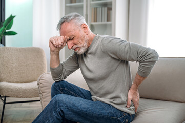 Old man sitting on couch and feeling sudden back pain