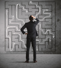 Confused business man seeks a solution to the labyrinth drawn on the wall
