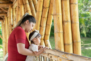 latina mother carrying her young daughter walking across a bamboo bridge while enjoying the scenery
