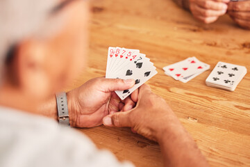 Hands, cards and a senior man playing poker at a table in the living room of a retirement home....