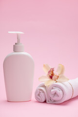 Obraz na płótnie Canvas Vertical studio shot of a white mockup bottle with cosmetic product and orchid flower on rolled tied white waffle towels