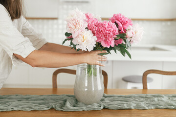 Woman arranging beautiful peonies in vase in new modern home. Young female decorating house with...