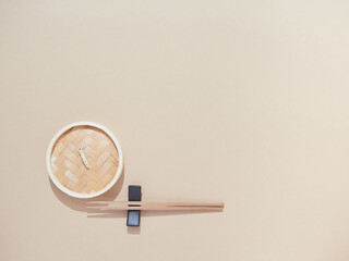 Asian kitchenware. Bamboo steamer and chopsticks placed on black support. Top view on sand-colored background with copy space.