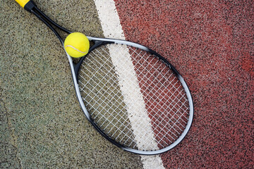 Closeup top view on tennis ball and racket racquet lying on acrylic tennis hard court surface with empty blank copy space.