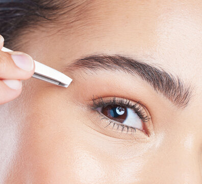 Closeup of a young woman tweezing her eyebrows in a studio for grooming or hair removal face routine. Skincare, beauty and zoom of female model doing a facial epilation treatment with metal tweezers.