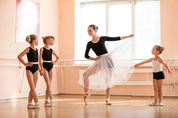 Young girl warming up and talking to younger classmates at ballet dancing class
