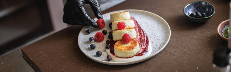 Kitchen worker decorated ready cheesecakes with berries for breakfast in restaurant