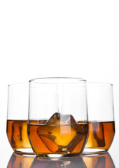 Glasses of whiskey with ice cubes with reflection on white background