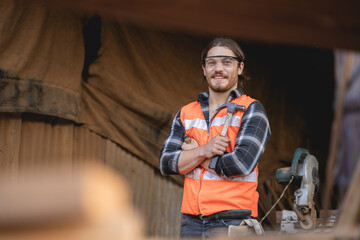 Young male carpenter working on design and cutting wood in the workshop, using a circular saw to cut a large board of wood on a wooden table in the workshop