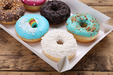 Box with different tasty glazed donuts on wooden table, closeup