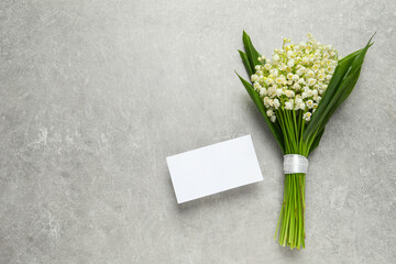 Beautiful lily of the valley bouquet and blank card on grey table, flat lay. Space for text