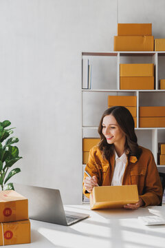 Business owner writing customer address on parcel boxes to deliver products to customers at home. Woman writing address on cardboard box at workplace. Small business entrepreneur SME.