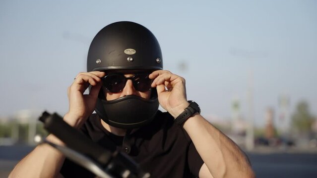A brutal look from a biker who put on sunglasses. Black safety helmet. A man in black clothes sits on his motorcycle.