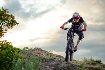 Professional Cyclist Riding the Bike Down Rocky Hill at Sunset. Extreme Sport Concept. Space for Text.