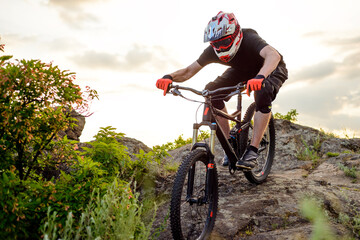 Fototapeta premium Professional Cyclist Riding the Bike Down Rocky Hill at Sunset. Extreme Sport Concept.