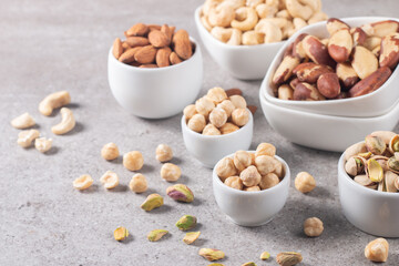 Large assortment of nuts in different bowls on stone table.