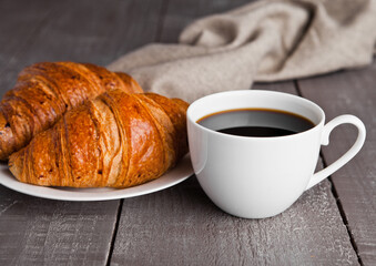 Cup of black coffee and croissant for breakfast on wooden background