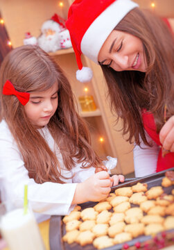 Mother with daughter making Christmas cookies, decorating gingerbread for festive dinner, celebrating winter holidays at home