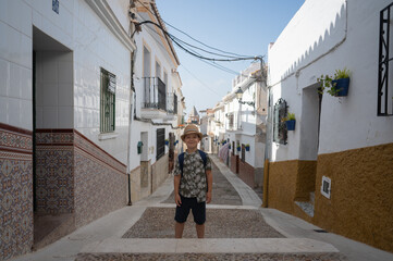 A boy tourist in a hat stands against a narrow street of the old town in Spain