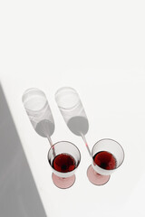 Minimal summer scene with glass of red wine, sunlight shadow on white background, copyspace, wineglass flat lay. Two wine glasses, alcohol drinks photo. Holidays, parties, events concept