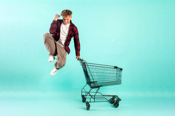 young crazy guy shopper jumps and rejoices with shopping cart from supermarket