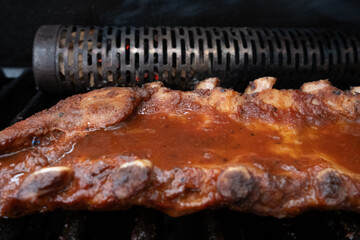 closeup of spareribs on a grill, with smoker and marinade