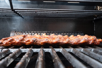 closeup of spareribs on a grill, with smoker and marinade