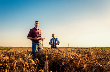 Portrait of two farmers standing in golden wheat field at sunset.