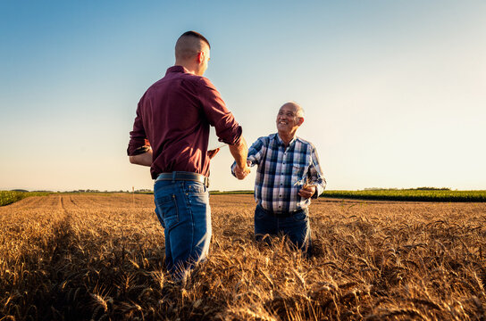 Two farmers in wheat field making agreement with handshake at sunset.
