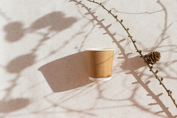 Eco friendly craft paper cup on pastel background with branch with cone and shadow. Recycling concept. Zero waste theme. Top view. Falt lay