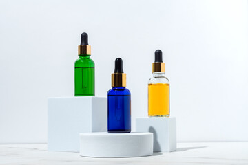 Face serum dropp bottles on white podiums on white background. Home routine skin care cosmetic set. Unbranded bottles for your design.
