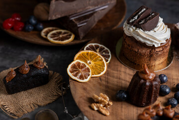 cakes puddings and chocolate muffins with blueberries and cream cherries and slices of dried citrus on highly decorated wooden plate.
