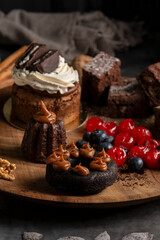 cakes puddings and chocolate muffins with blueberries and cream cherries and slices of dried citrus on highly decorated wooden plate.