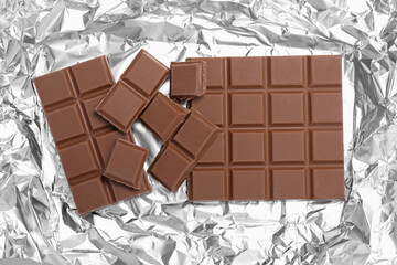 Pieces of delicious milk chocolate bars on foil, flat lay