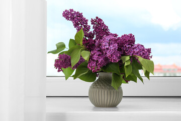 Beautiful lilac flowers in vase on windowsill