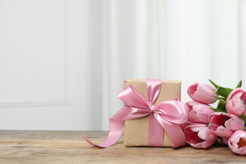 Beautiful gift box with bow and pink tulips on wooden table. Space for text