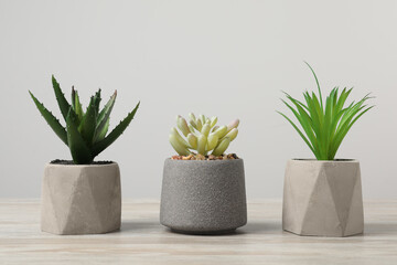 Many different artificial plants in flower pots on wooden table against light grey background