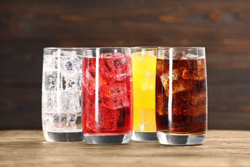 Glasses of different refreshing soda water with ice cubes on wooden table