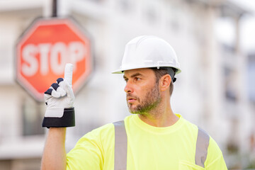 Worker builder in hard hat with stop road sign. Builder with stop gesture, no hand, dangerous on...